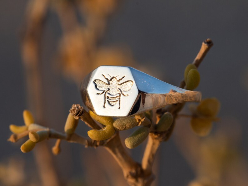 May include: A silver signet ring with a hexagonal face featuring an engraved bee design.