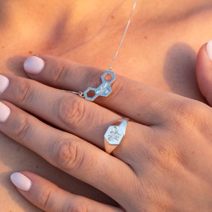 May include: A silver necklace with a honeycomb pendant featuring a bee design. A matching silver ring with a bee design is worn on a finger.