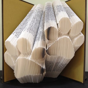 May include: A book folded into the shape of a paw print. The book is open and the pages are folded to create a three-dimensional effect. The book is on a brown surface.