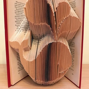Puede incluir: Una escultura de arte de libro hecha doblando las páginas de un libro en una forma tridimensional. La escultura tiene la forma de una flor con múltiples capas de páginas dobladas.