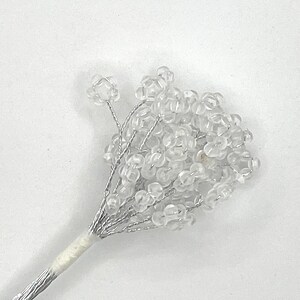 May include: A bunch of clear plastic beads on a silver wire stem. The beads are clustered together in a flower-like shape.