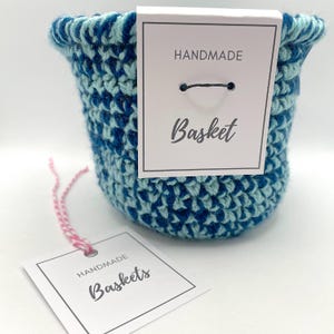 Pode incluir: Uma cesta de croch&ecirc; azul e verde com uma etiqueta branca que diz "Handmade Basket".
