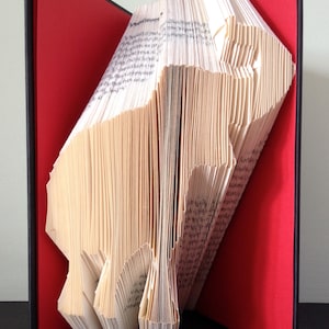 Op de afbeelding: Een boek gevouwen in de vorm van een beer, openstaand op een rode achtergrond. Het boek is gemaakt van wit papier met zwarte tekst.