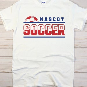 May include: White t-shirt with a red and blue graphic design that says "MASCOT SOCCER" with a soccer ball above the text.