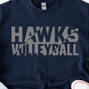 May include: Navy blue sweatshirt with the words "HAWKS VOLLEYBALL" printed in gray block letters. The text has a geometric design. The sweatshirt has a crew neck and long sleeves. The brand label is visible at the back of the neck.