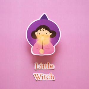 little witch wearing her purple witch hat and holding a magical glowing wand