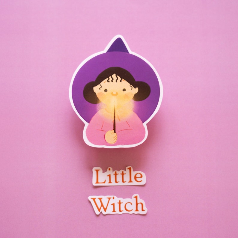 little witch wearing her purple witch hat and holding a magical glowing wand