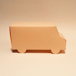 May include: A light peach-colored cardboard box shaped like a delivery truck. The box has a flat top and a rounded front with cut-out wheels.