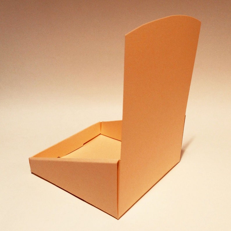 May include: A light peach-coloured cardboard box with a triangular base and a tall, rectangular back panel. The box is open and the back panel is folded down.