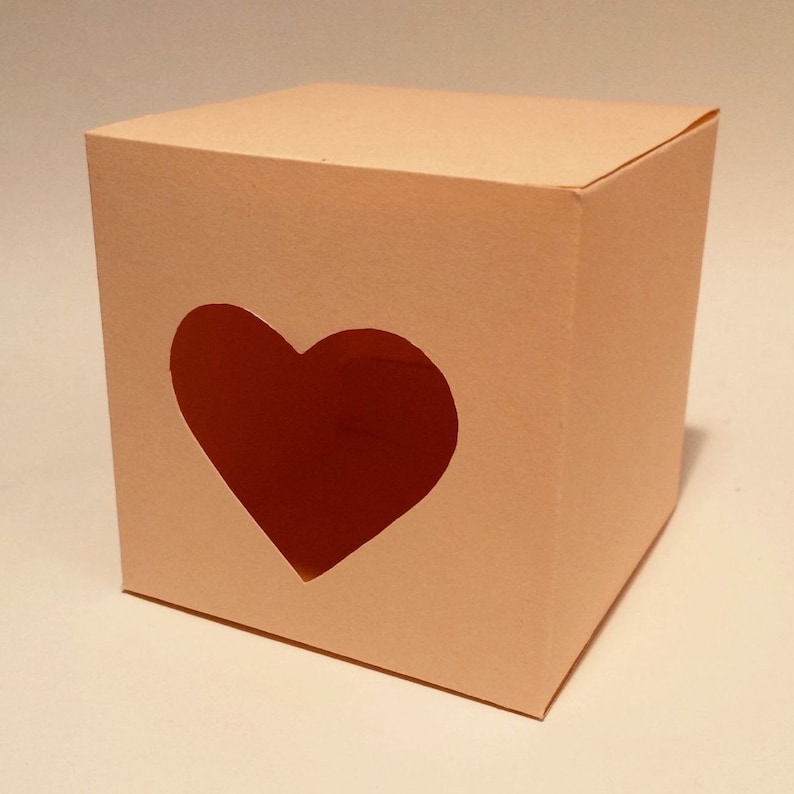 May include: A light pink cardboard box with a heart-shaped cutout. The box is empty.