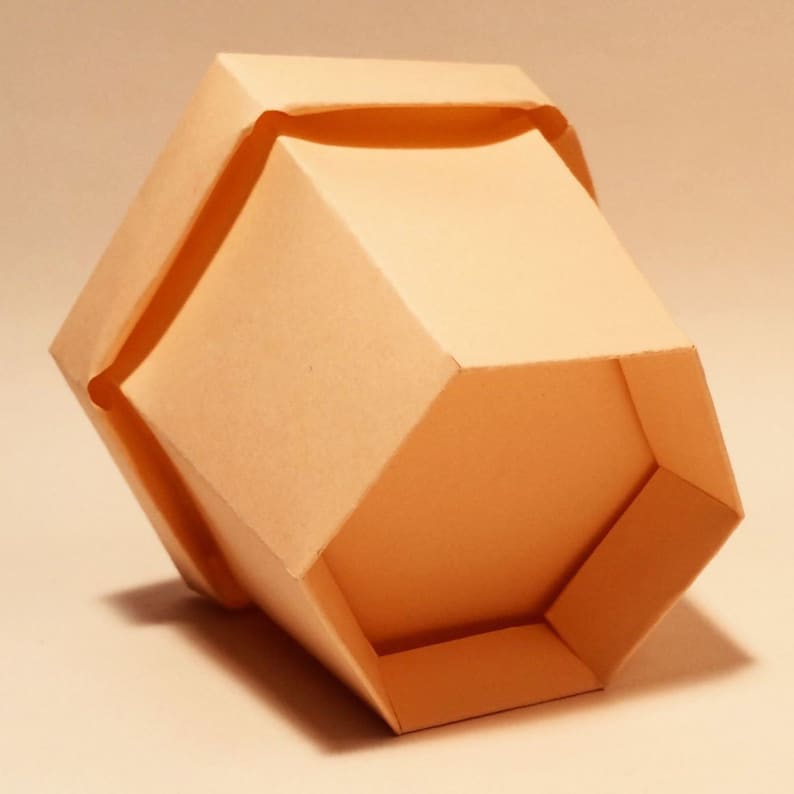 May include: A light brown hexagonal paper box with a folded top. The box is made of a thin, flexible material and has a smooth, matte finish.