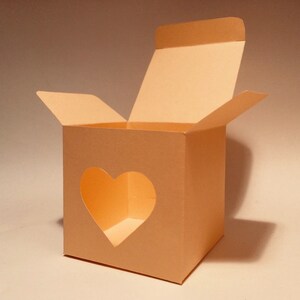 May include: An open peach-colored cardboard box with a heart-shaped cutout on the front. The box is designed for packaging small gifts or favors.