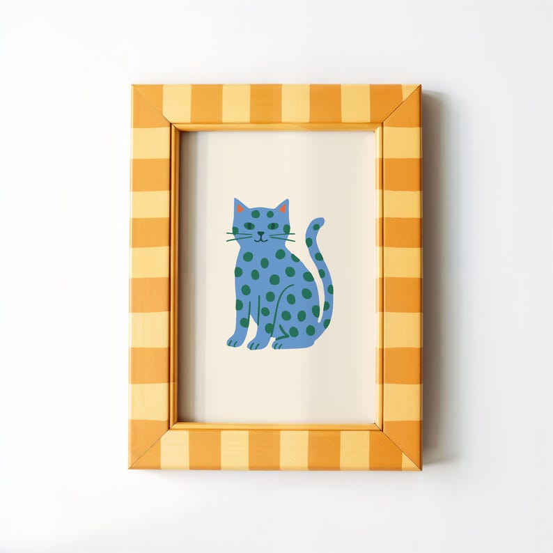 Puede incluir: Una impresi&oacute;n enmarcada de un gato azul con lunares verdes. El gato est&aacute; sentado sobre un fondo crema. El marco es amarillo y naranja con un dise&ntilde;o a rayas. La obra de arte es una ilustraci&oacute;n caprichosa.