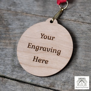 May include: A round wooden medal with a red ribbon attached. The medal is engraved with the text "Your Engraving Here".