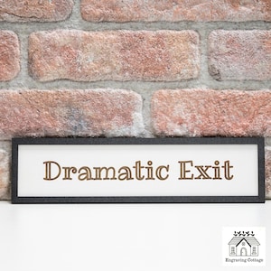 May include: A white sign with a black frame and the text "Dramatic Exit" in brown lettering.