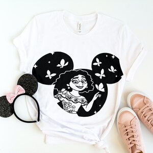 May include: White t-shirt with a black and white graphic of a girl with butterflies in a Mickey Mouse silhouette.