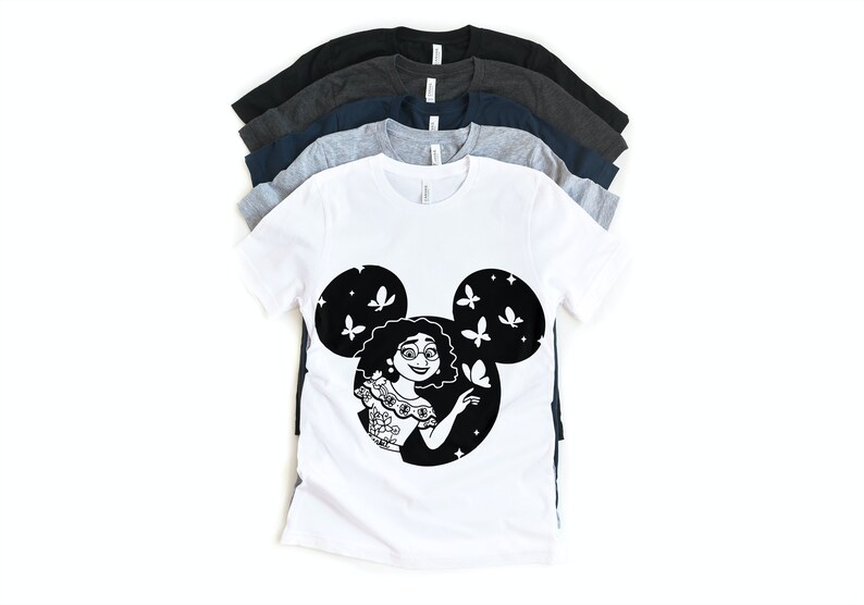 May include: A white t-shirt with a black silhouette of a woman with curly hair inside a Mickey Mouse head shape. The woman is wearing a floral patterned dress and has butterflies around her.