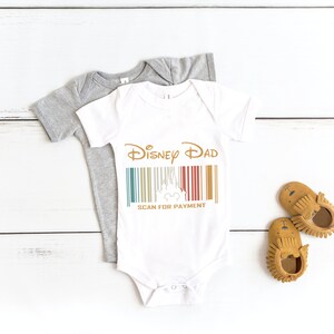 May include: White baby onesie featuring the text "Disney Dad" and a barcode with a Mickey Mouse head. The barcode has a retro colour scheme of red, yellow, blue, and green. The text "Scan for Payment" is below the barcode.