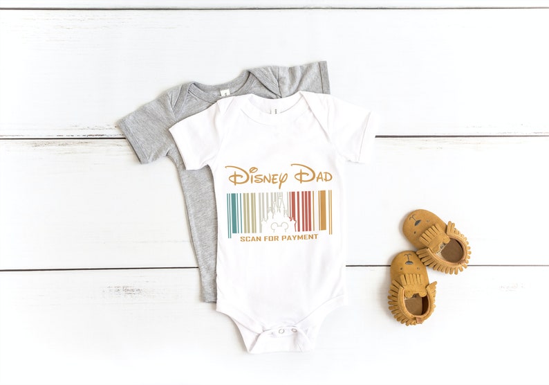 May include: White baby onesie featuring the text "Disney Dad" and a barcode with a Mickey Mouse head. The barcode has a retro colour scheme of red, yellow, blue, and green. The text "Scan for Payment" is below the barcode.