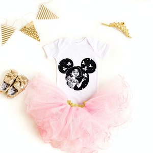 May include: A white baby onesie with a black Mickey Mouse silhouette featuring a cartoon character with butterflies. The onesie is paired with a pink tulle tutu and gold shoes.
