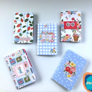 May include: Five small notebooks with different floral and patterned covers. The covers feature strawberries, gingham, flowers, and a bicycle. The text on the covers includes "You are the sweetest", "The best summer memories", "Summer vibes", and "Think + Make".