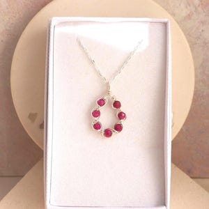 May include: A silver-toned necklace featuring a teardrop-shaped pendant constructed from thin wire wrapped around six small, round, vibrant pink beads. The necklace is presented inside a rectangular white box with a soft, padded interior lining.