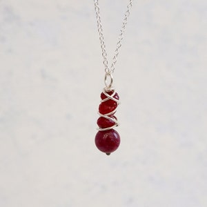May include: A silver chain necklace with a pendant made of three red gemstone beads wrapped in silver wire.