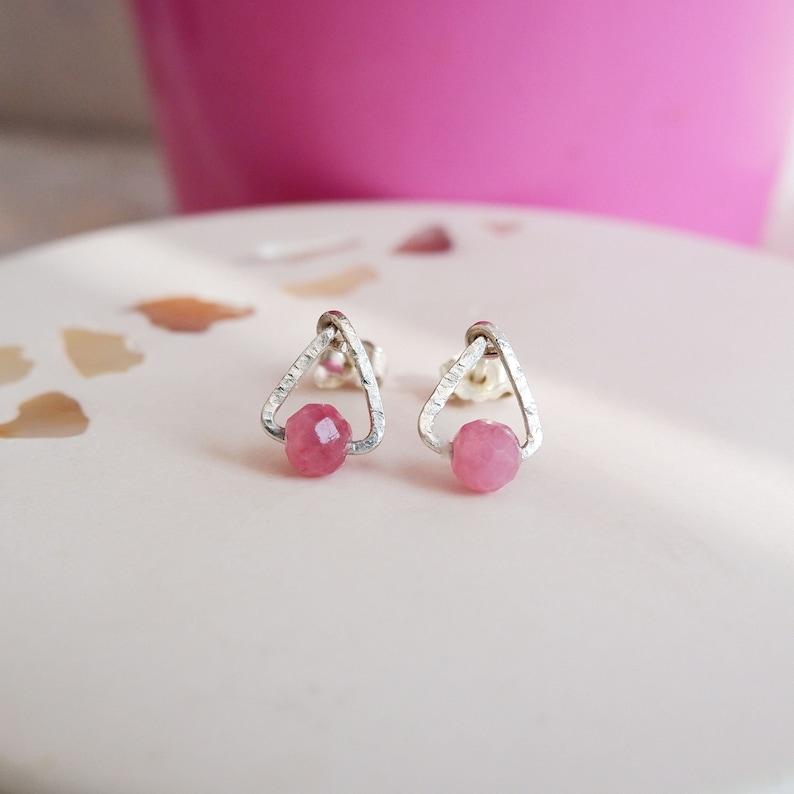 May include: A pair of silver triangle stud earrings with pink gemstone accents.