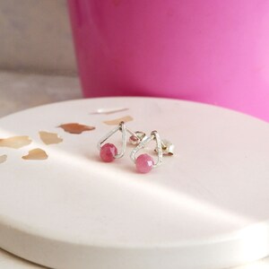 May include: A pair of silver earrings with pink gemstone accents. The earrings feature a delicate, open triangle design.