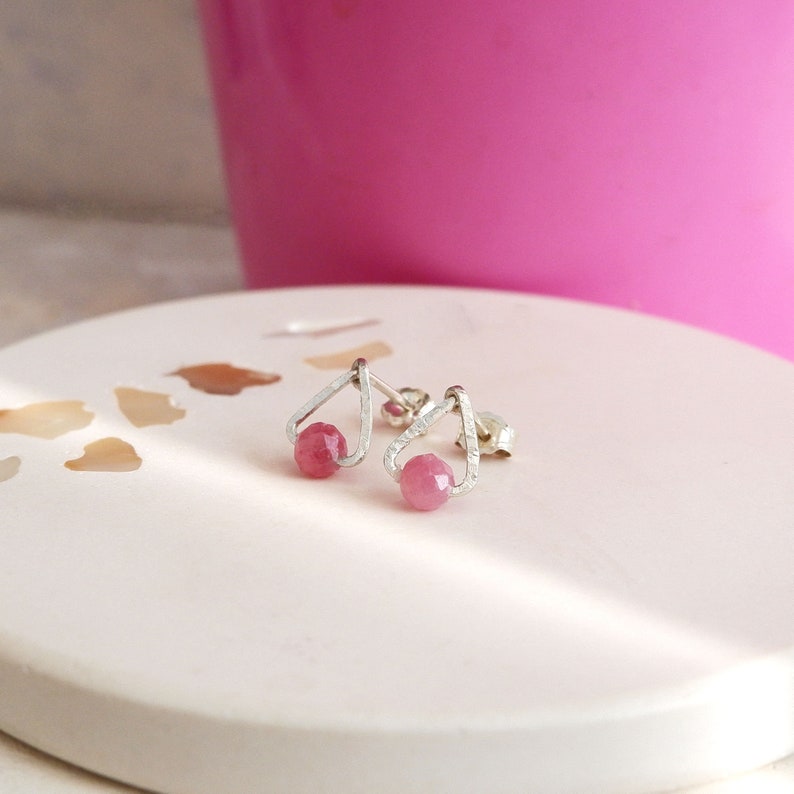 May include: A pair of silver earrings with pink gemstone accents. The earrings feature a delicate, open triangle design.