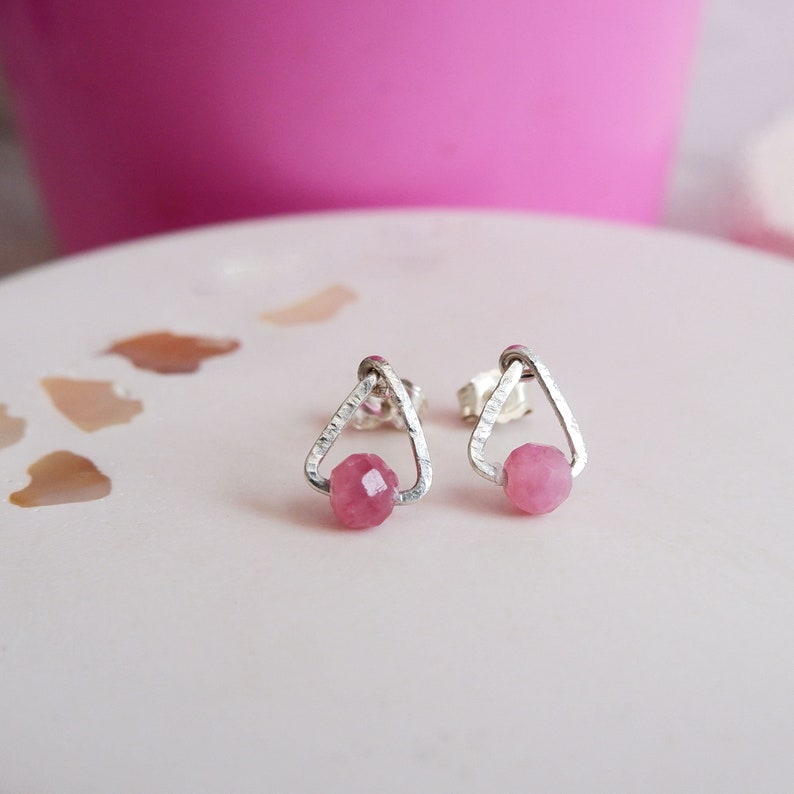 May include: A pair of silver triangle stud earrings with pink gemstone accents.