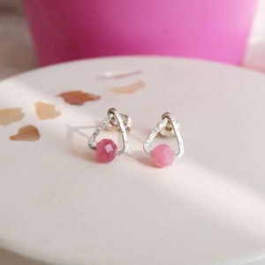 May include: A pair of silver triangle stud earrings with pink gemstone accents.