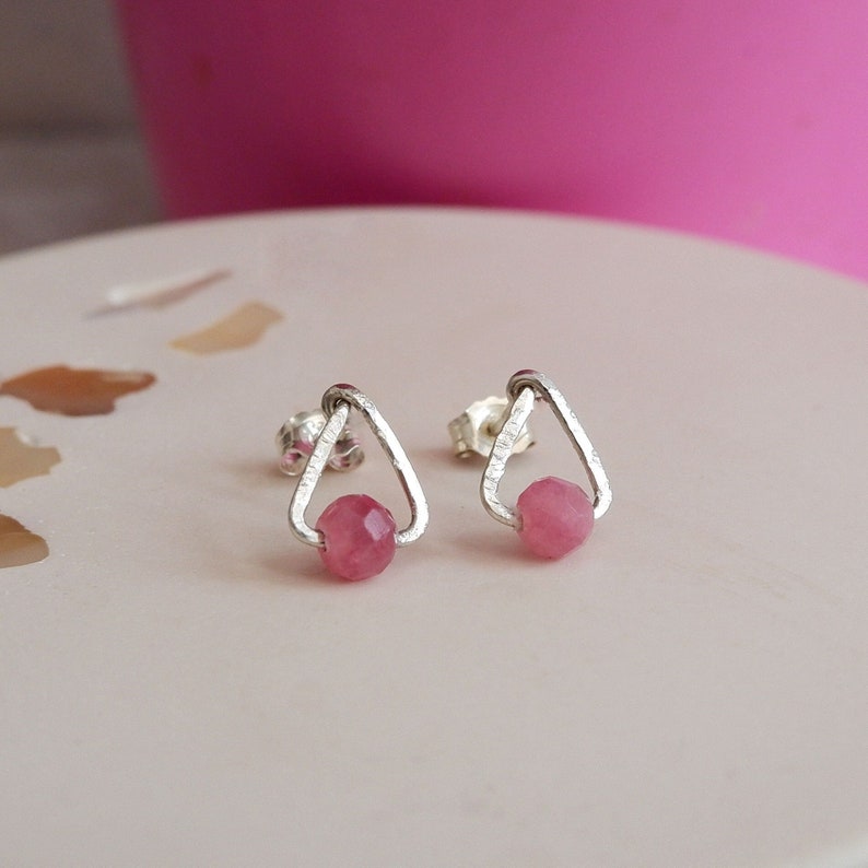 May include: A pair of silver triangle stud earrings with pink gemstone accents.