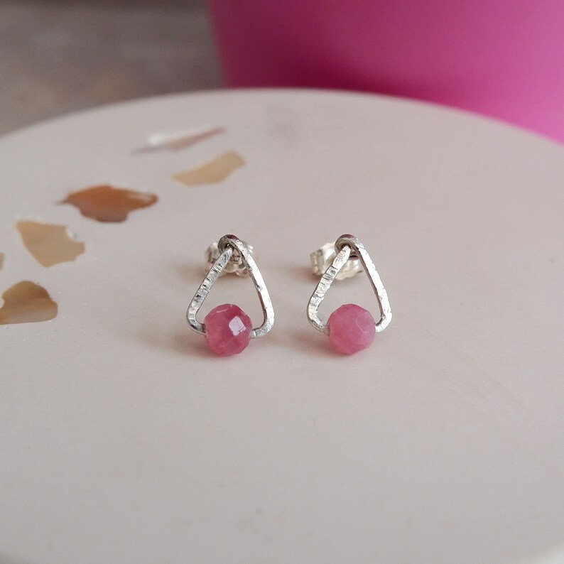 May include: A pair of silver triangle stud earrings with pink gemstone accents.