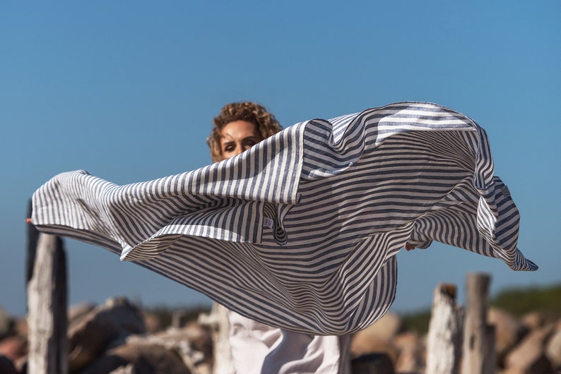 May include: A person wearing a white and blue striped shirt, with the shirt billowing in the wind.