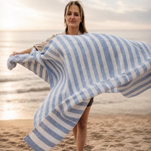 Woman holding a lightweight blue and white striped 100% linen beach towel on a beach at sunset