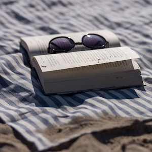 May include: A white book with a pair of black sunglasses on top of it, lying on a blue and white striped beach blanket.