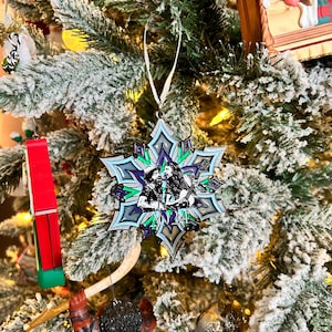 May include: A snowflake-shaped Christmas ornament with a purple, green, and blue design. The ornament features a stylized image of two people with the year 2024 printed on it.