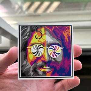 May include: A colorful sticker featuring a portrait of a man with a psychedelic swirl pattern in his glasses. The left side of the image is in shades of gray and black, while the right side is in shades of pink, purple, and blue.