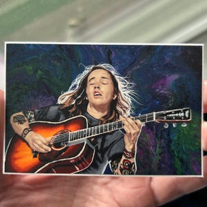 May include: A man with long, flowing hair plays an acoustic guitar. He is wearing a black shirt and has a tattoo on his arm. The background is a swirling, abstract design in shades of blue, green, and purple.