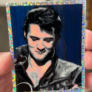 May include: A black and white portrait of a man with dark hair, wearing a black leather jacket. The background is a blue and white abstract design.