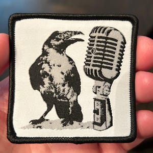 May include: Square patch with a black border featuring a black and white illustration of a crow and a vintage microphone. The crow is facing left, and the microphone is on the right. The patch is on a white background.