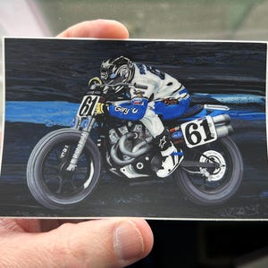 May include: A blue and white motorcycle with the number 61 on the side. The motorcycle is being ridden on a dirt track. The rider is wearing a blue and white racing suit and a helmet.