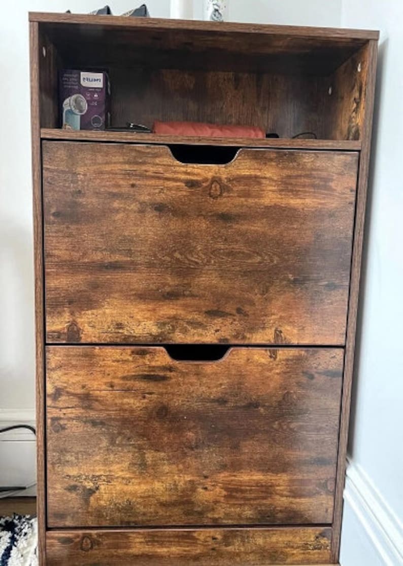 May include: A brown wooden shoe storage cabinet with two drawers and a top shelf. The cabinet has a distressed wood finish.