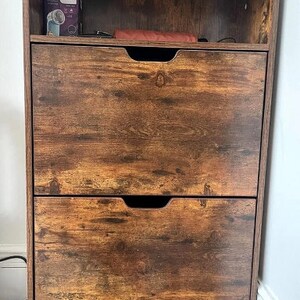 May include: A brown wooden shoe storage cabinet with two drawers and a top shelf. The cabinet has a distressed wood finish.
