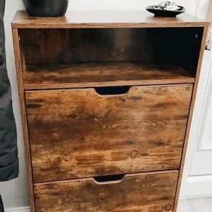 May include: A brown wooden shoe rack with three drawers and an open shelf. The shoe rack has a distressed wood finish.