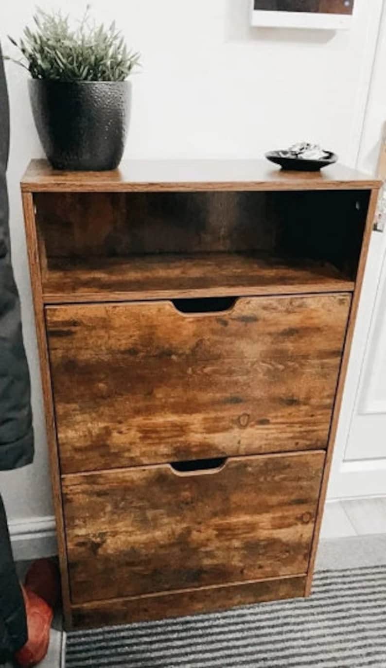 May include: A brown wooden shoe rack with three drawers and an open shelf. The shoe rack has a distressed wood finish.