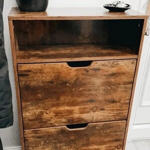 May include: A brown wooden shoe rack with three drawers and an open shelf. The shoe rack has a distressed wood finish.