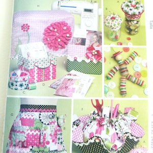 May include: A page from McCall's Crafts featuring sewing-themed projects. The image showcases a sewing machine cover, storage boxes, an apron, pincushions, and a fabric basket. The color palette includes pink, green, and white, with floral and polka dot patterns.