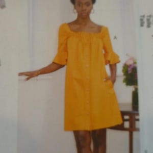 May include: A woman wearing a bright orange dress with a square neckline, button-down front, and short, flared sleeves. The dress has pockets and falls to the knees. The image is from a McCall's sewing pattern.